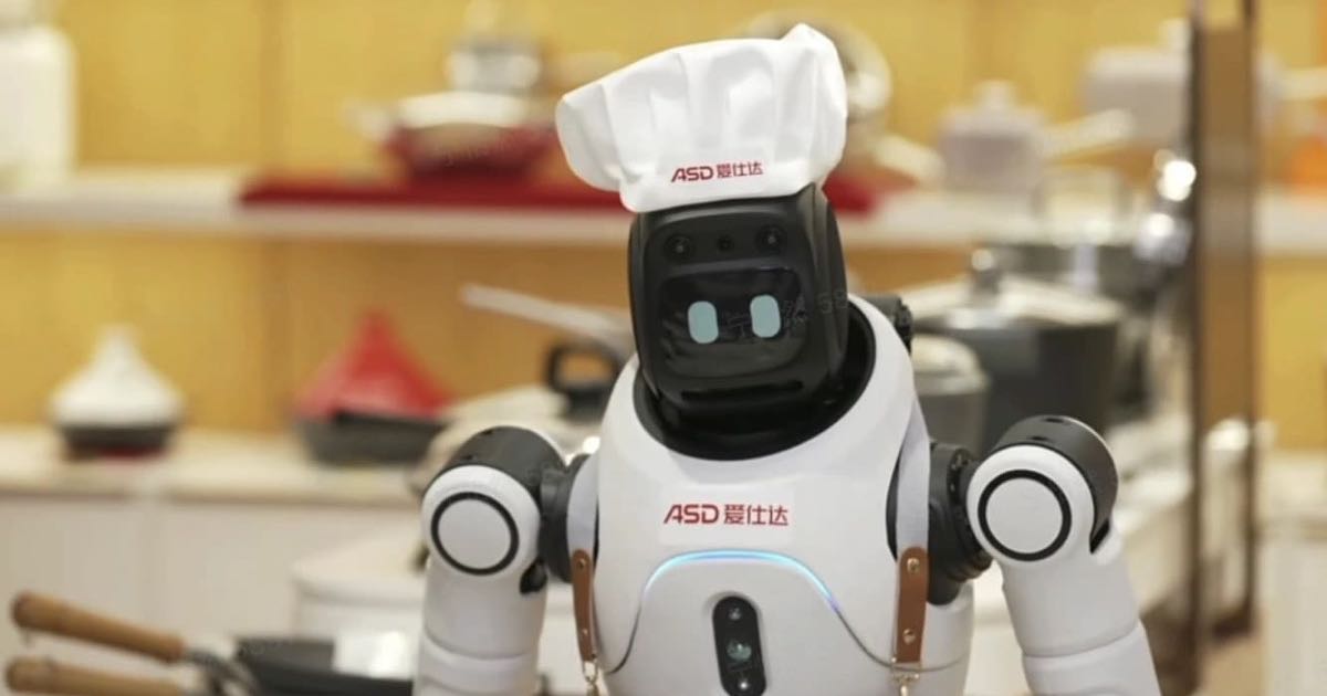 AGIBOT's X2 humanoid robot wearing an ASD-branded chef's hat and apron stands in front of cookware shelves in a retail store