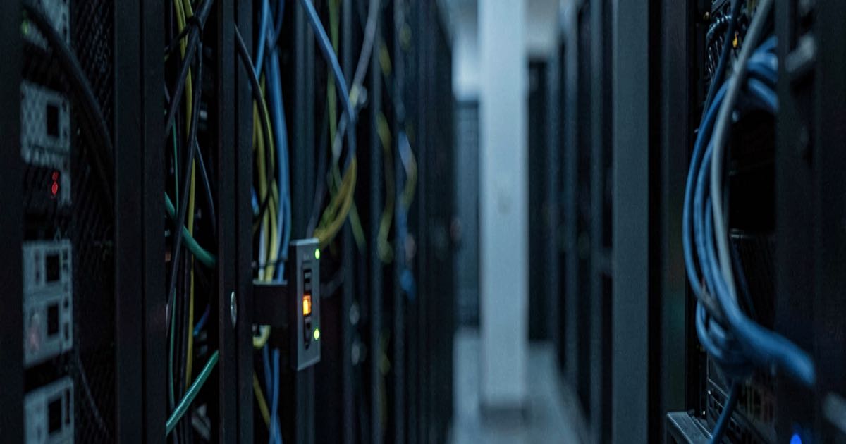 A dimly lit server room with a tangle of network cables and a glowing switch, documentary style, shallow depth of field.