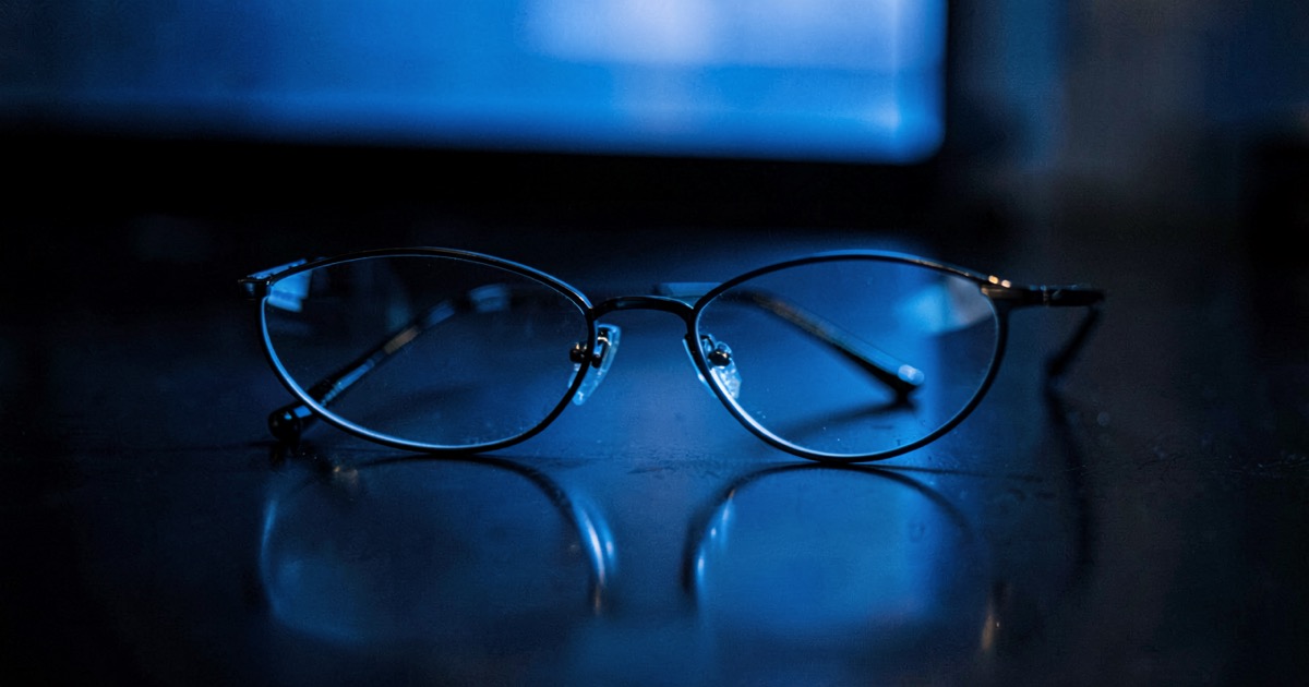 A pair of smart glasses resting on a dark polished desk surface with subtle blue light reflection