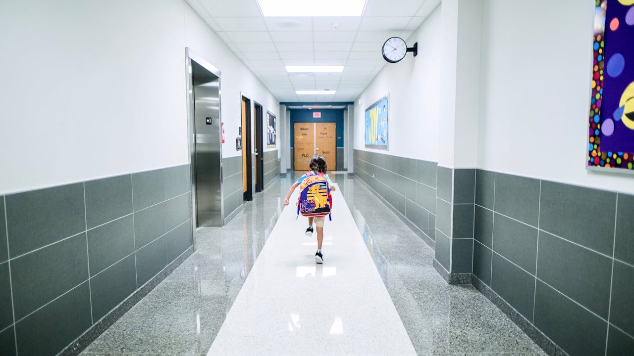 A school hallway with security cameras and students walking, muted lighting, documentary style