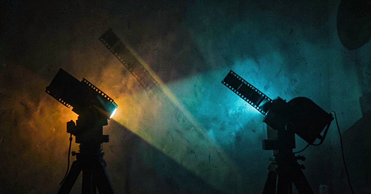 Abstract cinematic composition of two overlapping colored light beams from film projectors, one amber one cyan, on a dark wall with atmospheric haze