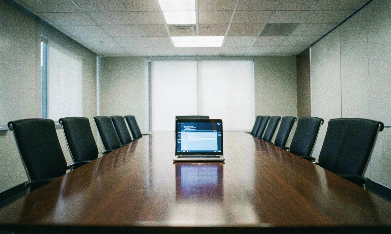 A corporate boardroom with empty chairs around a long table and a single glowing laptop, muted colors, documentary photography