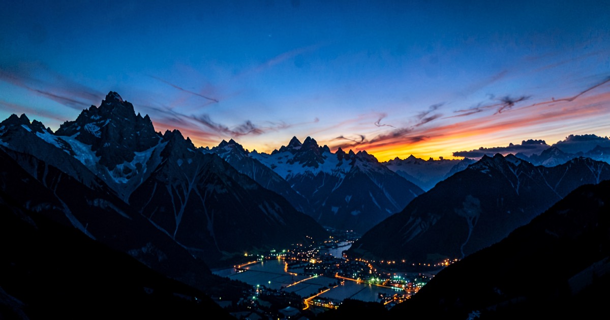 Dramatic alpine mountain silhouette at dusk with data center lights glowing in the valley below