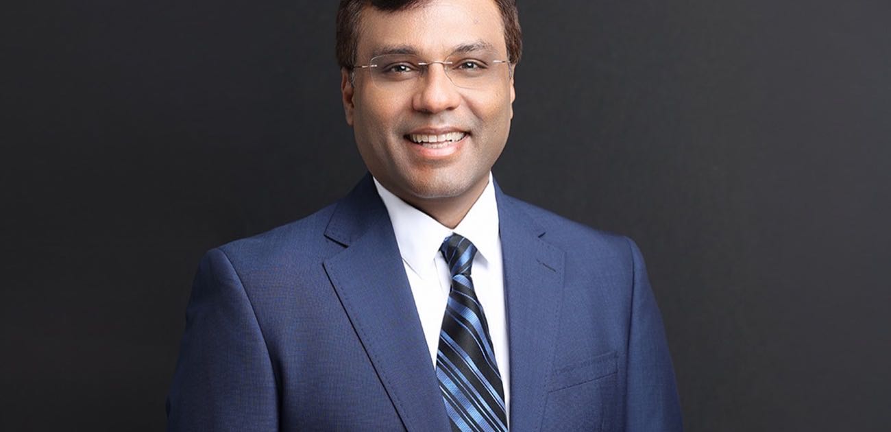 Rohit Prasad, incoming Boston Dynamics chief executive, in a blue suit and rimless glasses smiling against a dark background in a corporate headshot