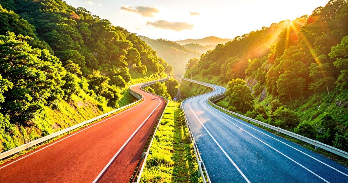 Two parallel racing tracks winding through a bright sunlit valley, one red and one blue, converging toward a shared finish line on the horizon.