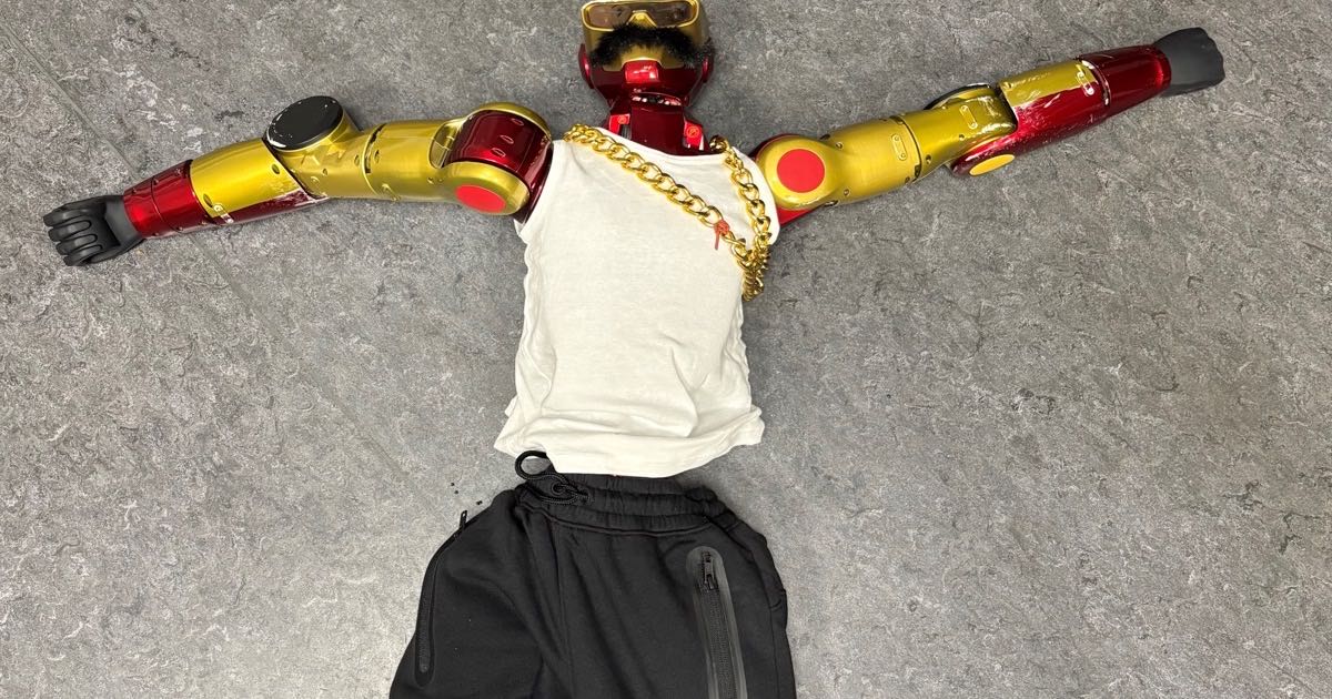 A red-and-gold humanoid robot with a fake moustache, white tank top, gold chain and sunglasses lies spread out on a grey tiled floor in a photos released by Cologne police after the machine was seized as evidence.