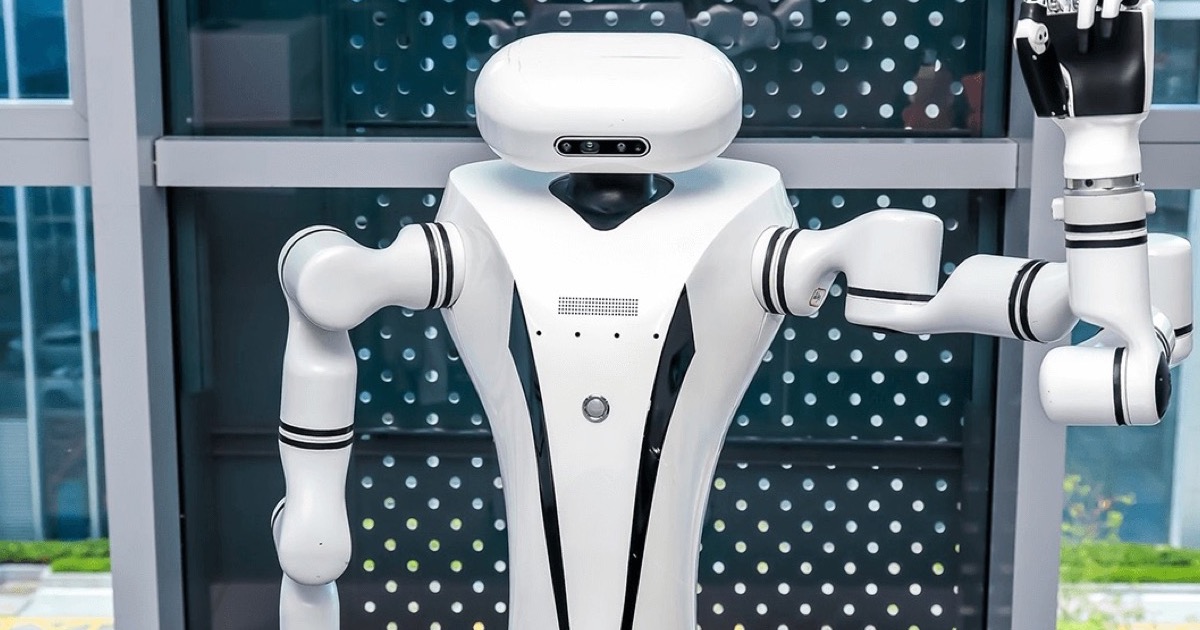 A white humanoid robot torso with both arms extended stands in a modern office lobby, one hand making a peace sign