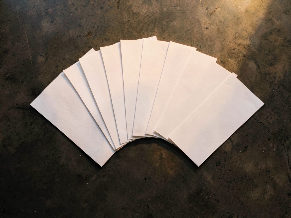 An overhead composition of blank paper sheets fanned out in a semicircle on a dark concrete surface, soft golden lighting