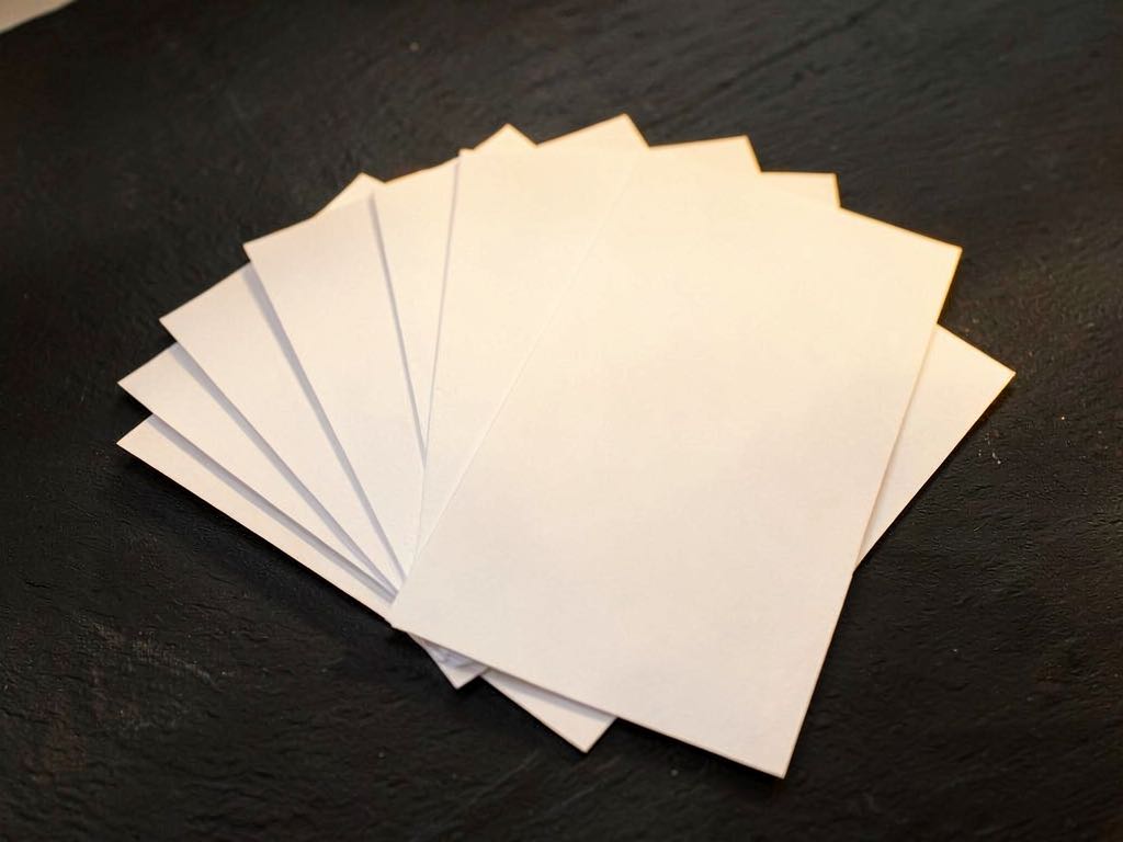 An overhead composition of blank paper sheets fanned out in a semicircle on a dark concrete surface, soft golden lighting