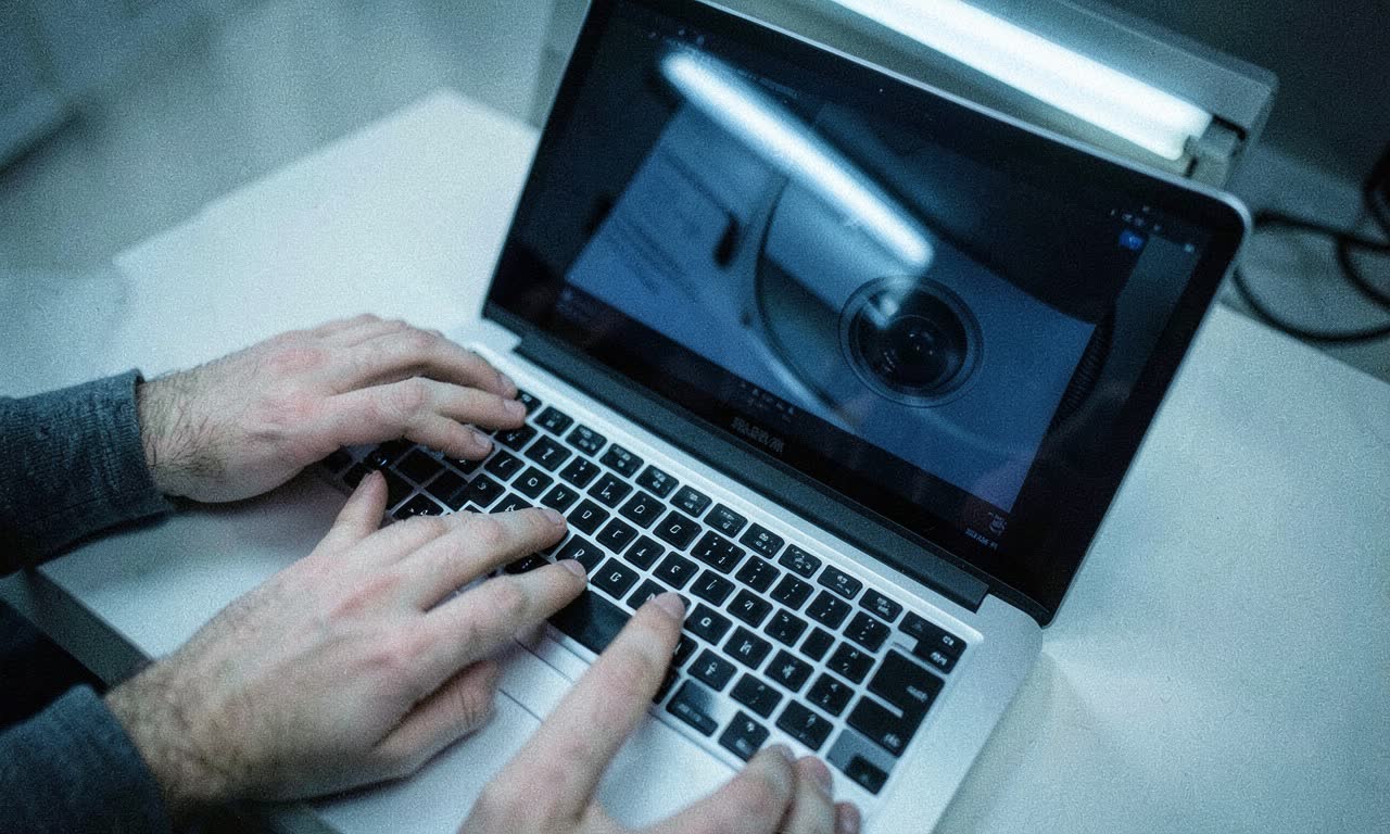 Overhead view of a person typing on a keyboard with surveillance camera lens reflection, cold fluorescent lighting, document style