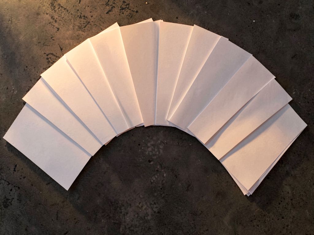 An overhead composition of blank paper sheets fanned out in a semicircle on a dark concrete surface, soft golden lighting