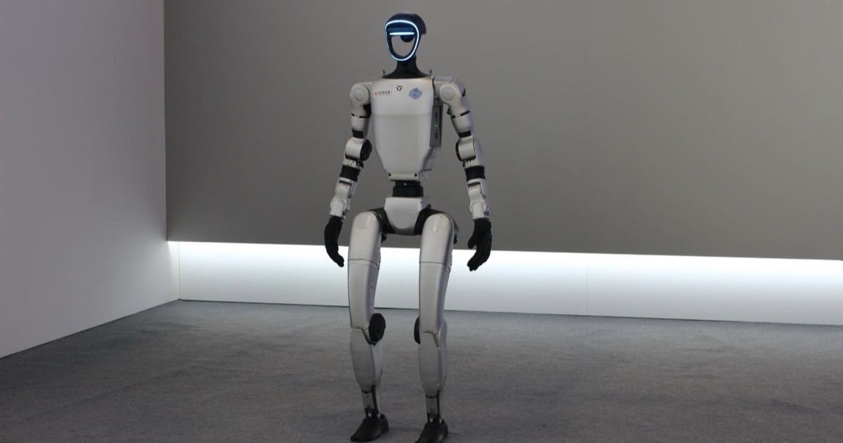 Dongfeng's white Xiaodong humanoid robot stands on a grey stage, a dark visor wrapping its head above a slim two-legged frame.