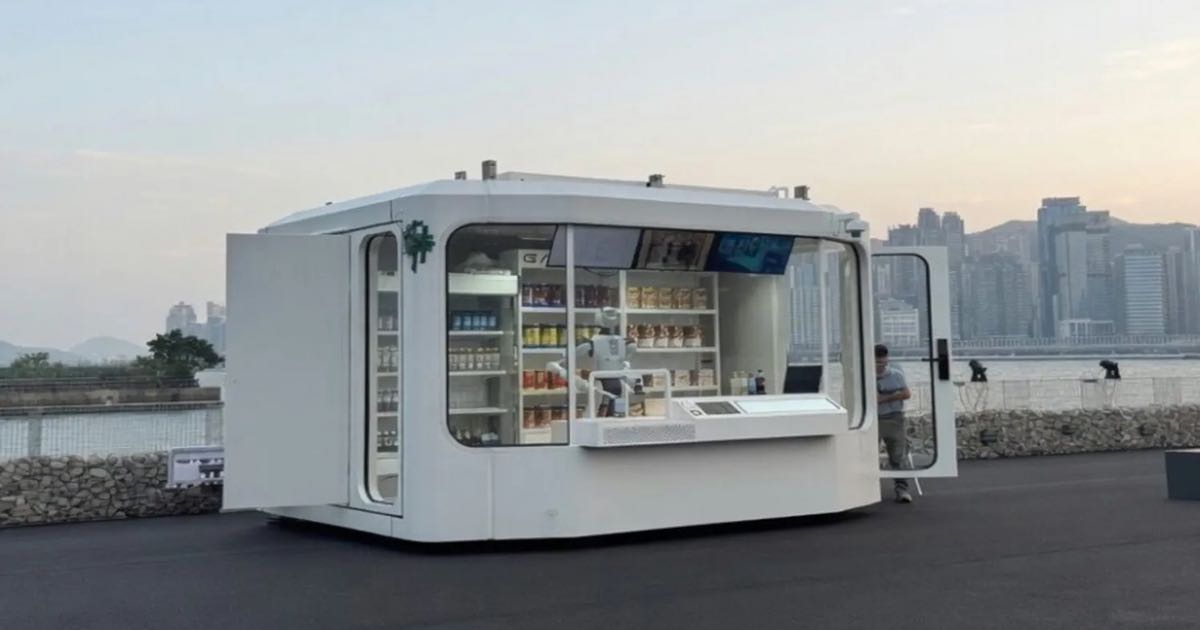 A white capsule-shaped Galbot convenience store on Hong Kong's Hung Hom waterfront, with the G1 humanoid robot visible inside behind the counter at dusk.