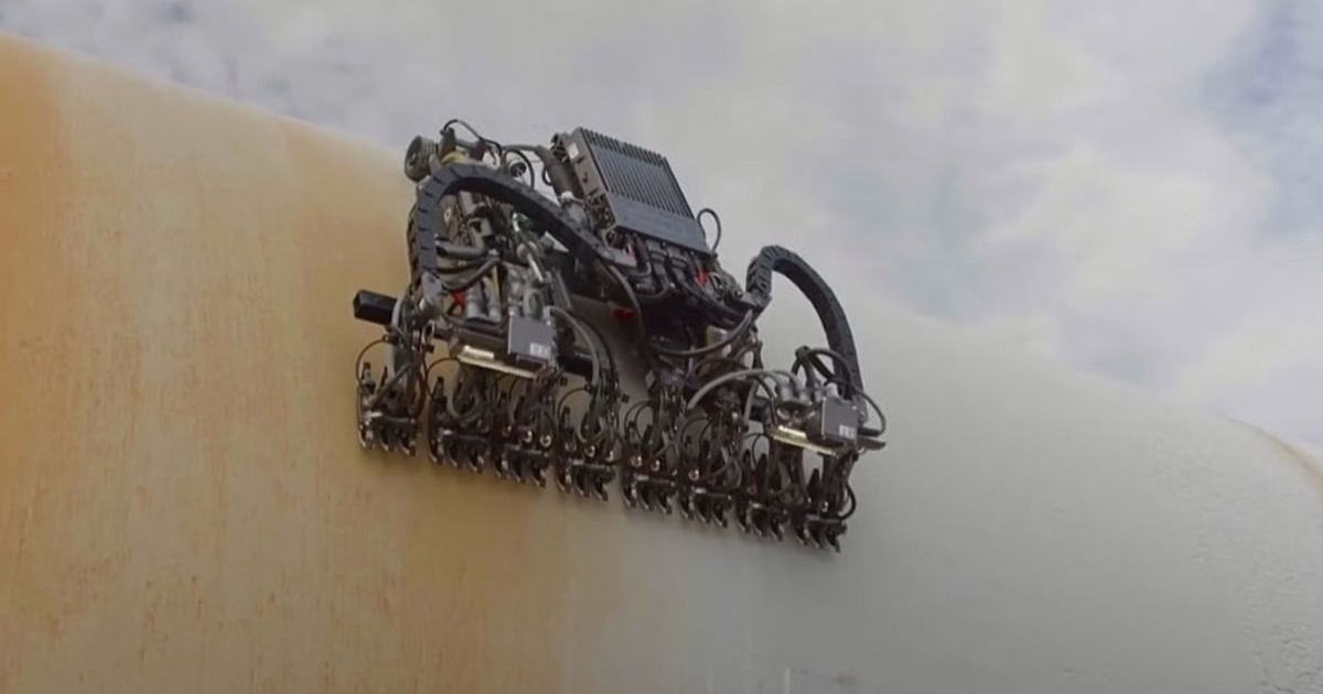 A Gecko Robotics wall-climbing inspection robot with a row of scanner feet crawling across a curved ship hull streaked with rust.