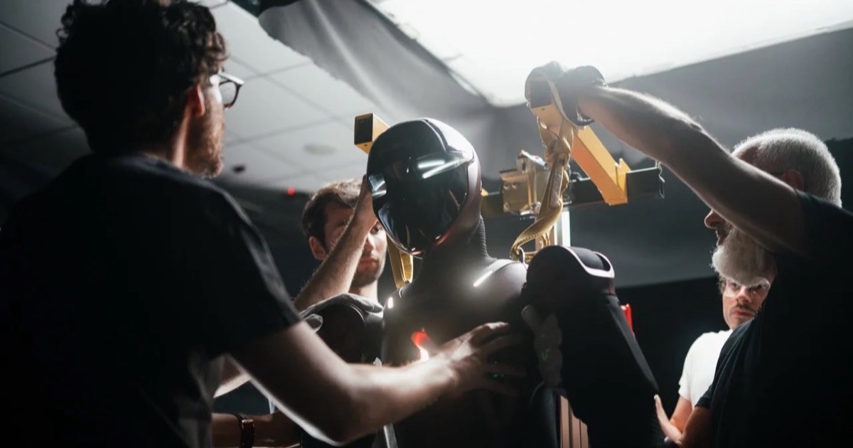 The Generative Bionics GENE.01 humanoid robot suspended in a studio rig while engineers adjust it during a development photoshoot