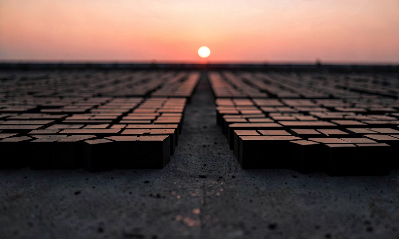 Abstract composition: rows of identical dark silicon wafers in silhouette against an amber-pink dusk sky, no markings visible