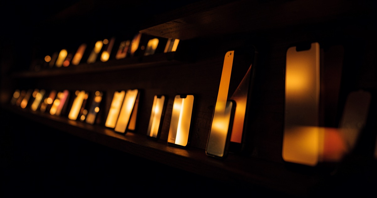 A dark room with rows of iPhones mounted on shelves, screens glowing in unison.