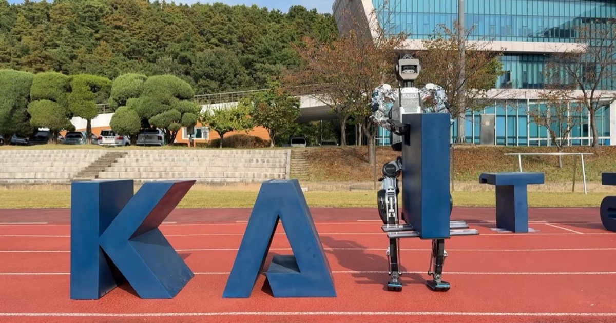 The KAIST Humanoid v0.9 robot pushing a large blue letter block across a running track on the KAIST campus.