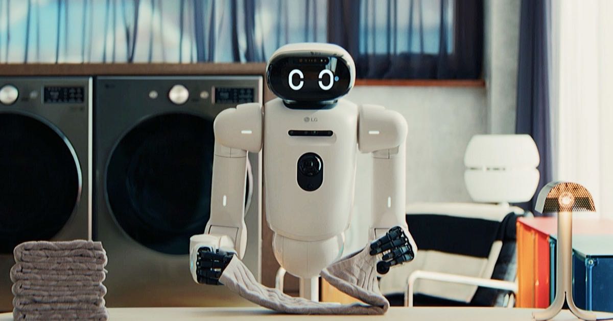A humanoid robot prototype in a bright modern factory setting, with AI computing infrastructure visible in the background.