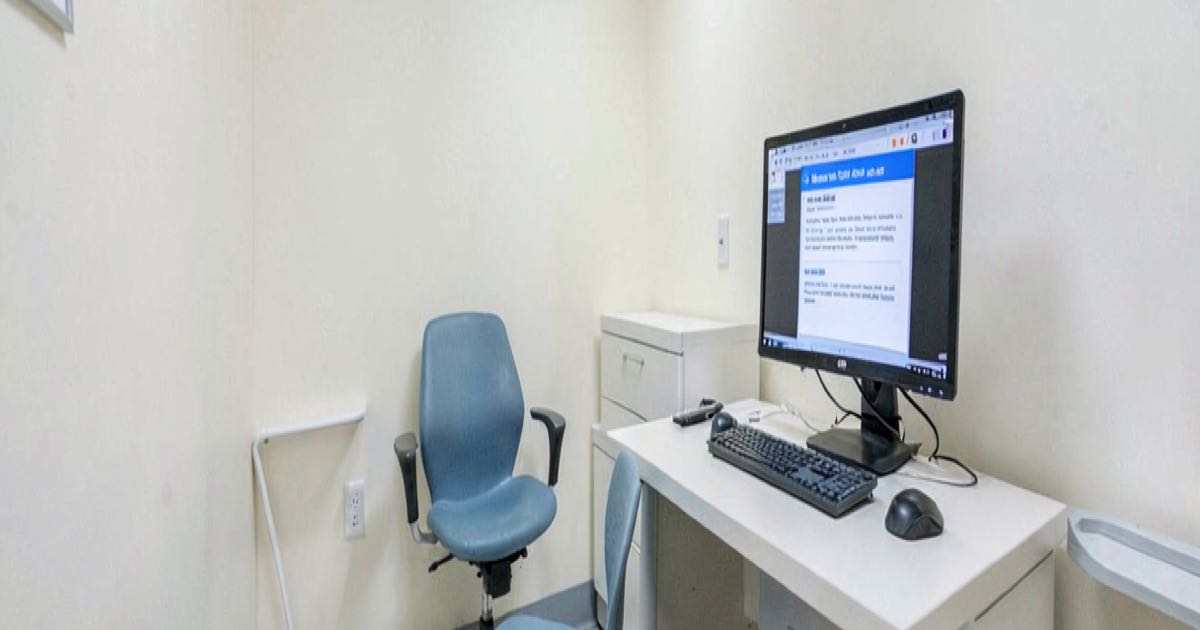 A medical waiting room with an empty appointment chair and a computer screen showing a prior authorization denial notification