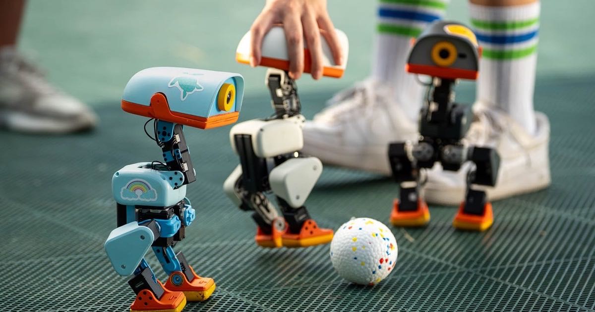 Three Microduck robots from Hugging Face and Pollen Robotics standing on a platform with a small white ball between them