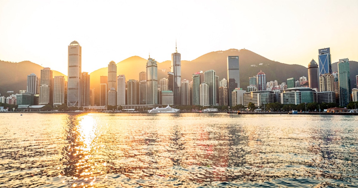 A bright modern Hong Kong harbour at golden hour with warm light reflecting on the water, no people, no text.