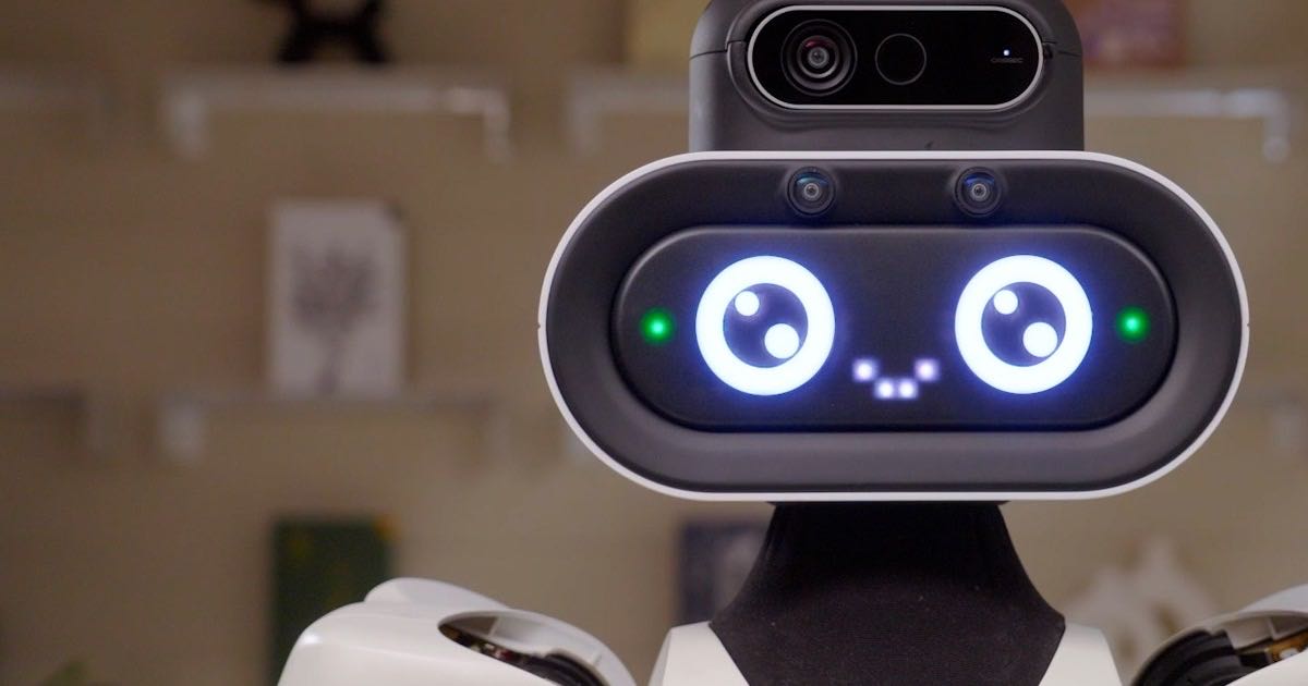 Close-up of Robot.com's R-noid humanoid robot, its face a dark screen with large illuminated cartoon eyes