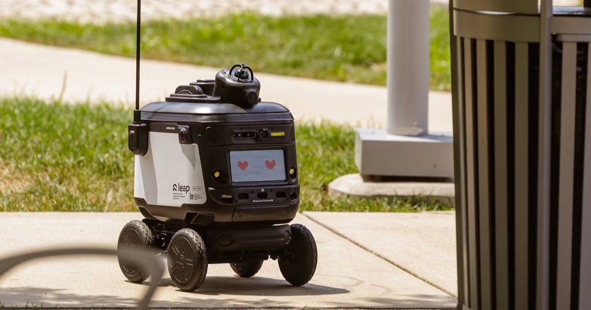 Robot.com's R-Kiwi sidewalk delivery robot crossing a campus footpath