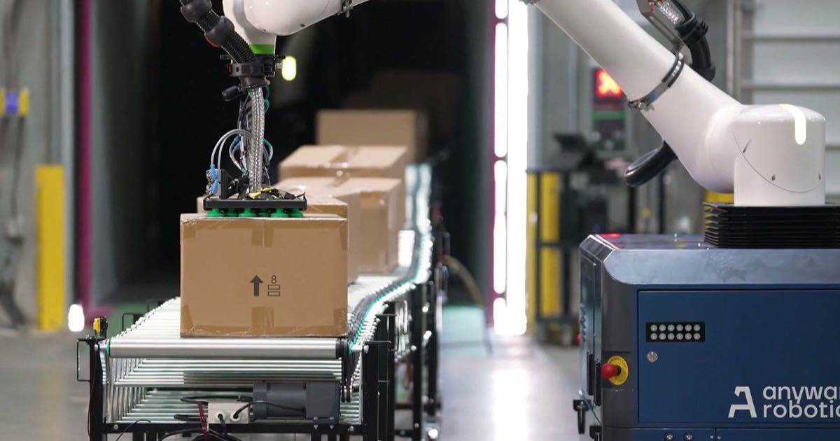 A robotic arm lifting a cardboard box from a conveyor belt in an automated warehouse facility