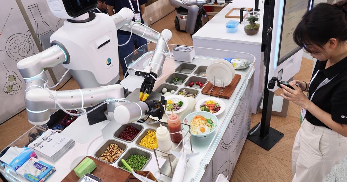 A humanoid robot standing in a warehouse environment alongside human workers.
