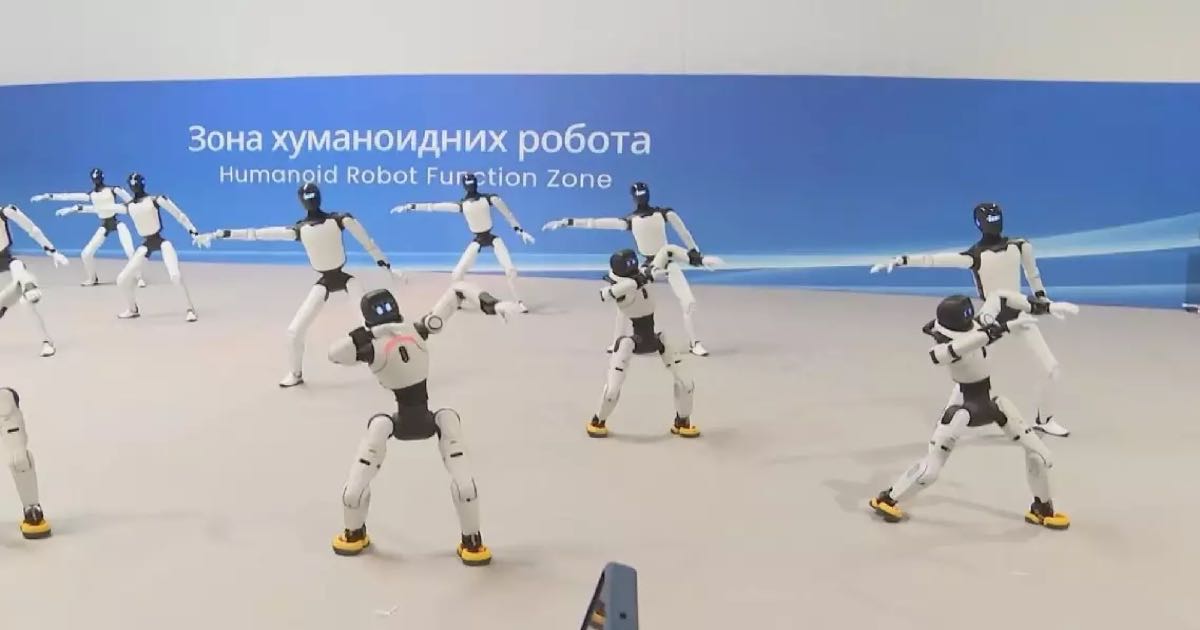 A group of white-and-black humanoid robots performing a synchronised demonstration at a humanoid robot exhibition zone in Serbia, with Serbian signage in both Cyrillic and English.
