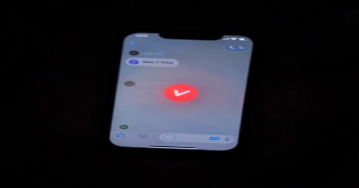 A smartphone screen showing a messaging app with a subtle red warning indicator overlay, dark background, soft glow from the screen, documentary photography style, no text no logos no letters no signs