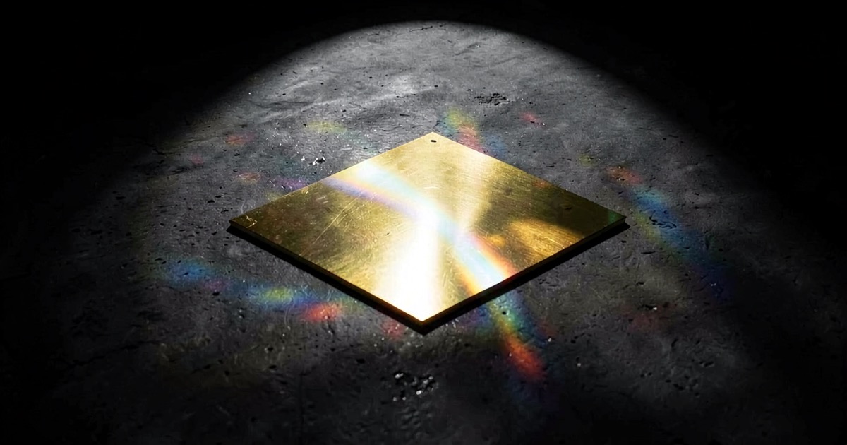 A golden semiconductor wafer on dark polished concrete under dramatic spotlight with refracted rainbow light patterns