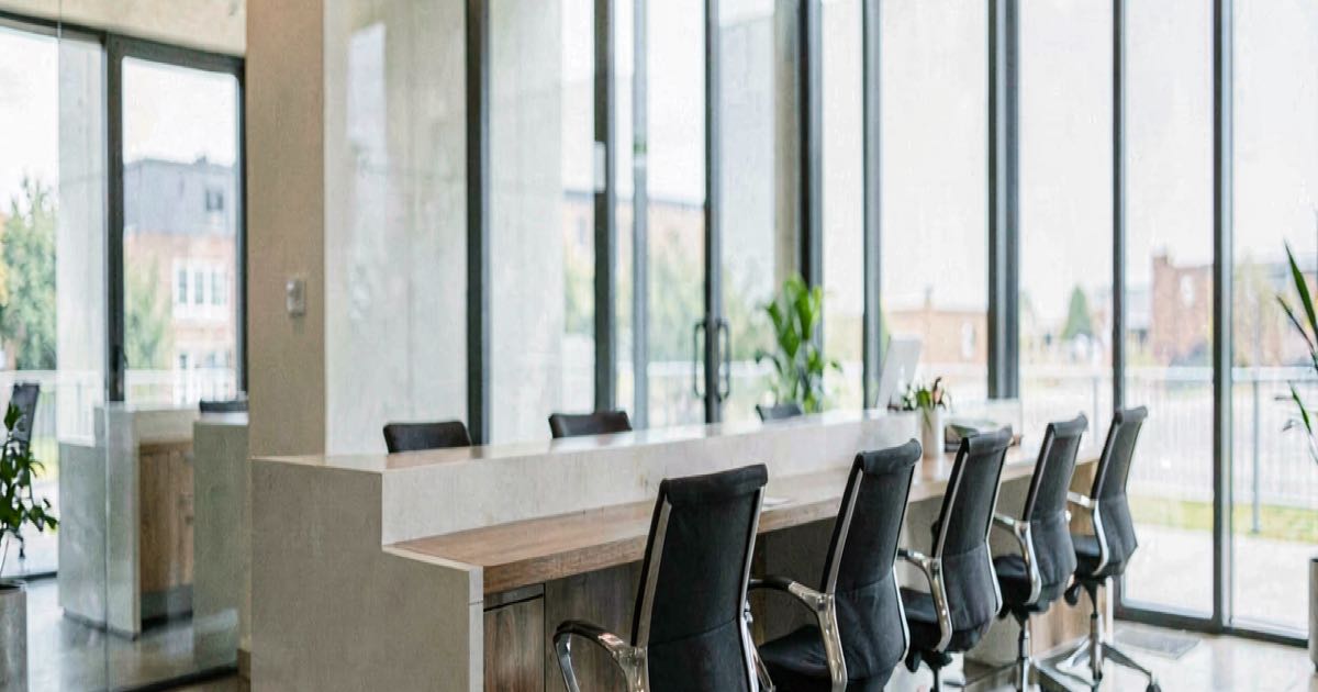 A modern office lobby with empty chairs at a reception desk, natural light streaming through glass walls.