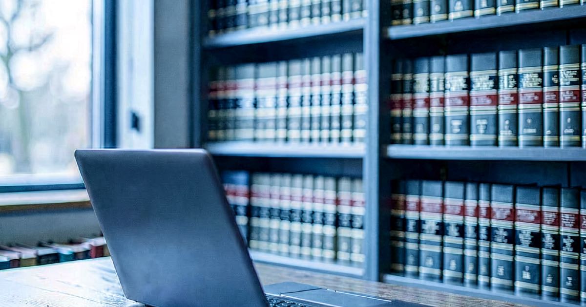 A modern law library with shelves of legal volumes and a laptop on a desk, lit by natural window light.