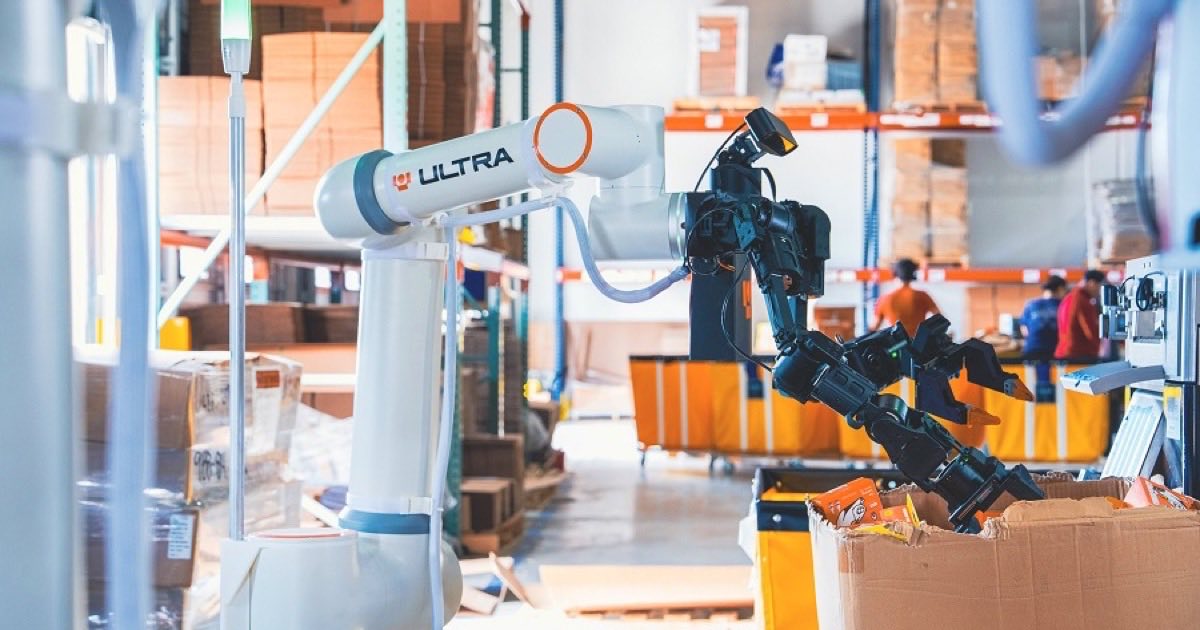 The Ultra Robotics OP1 Operator, a humanoid-style picking robot mounted on a robotic arm atop a wheeled flat base, standing in a warehouse