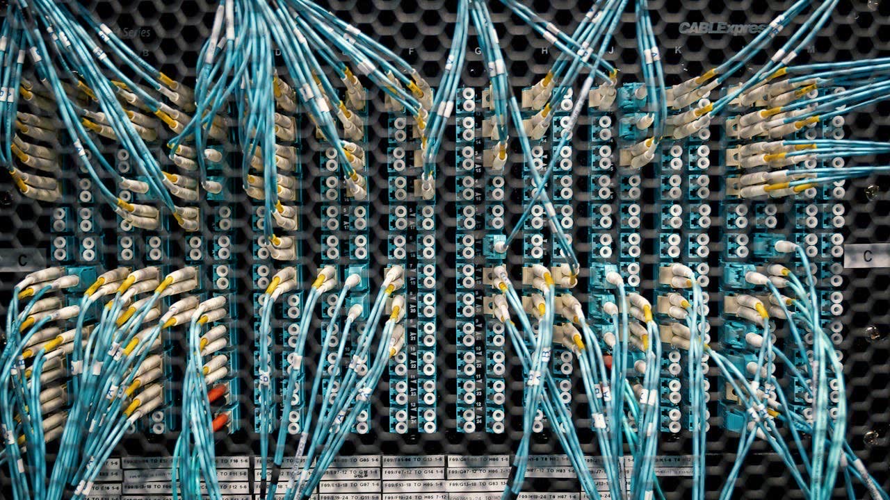A submarine cable landing station on a dark coastline, fiber optic cables running into the sea under overcast skies