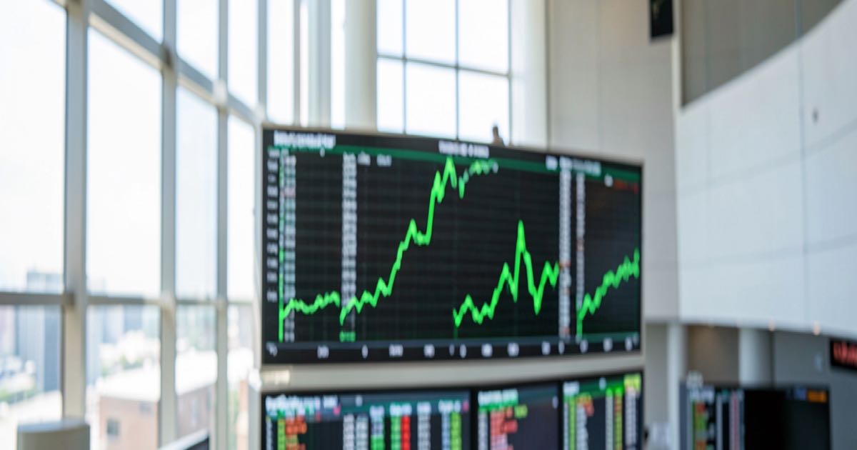 A modern stock exchange trading floor with electronic ticker boards showing a surging green line, bright daylight from floor-to-ceiling windows, editorial photography style