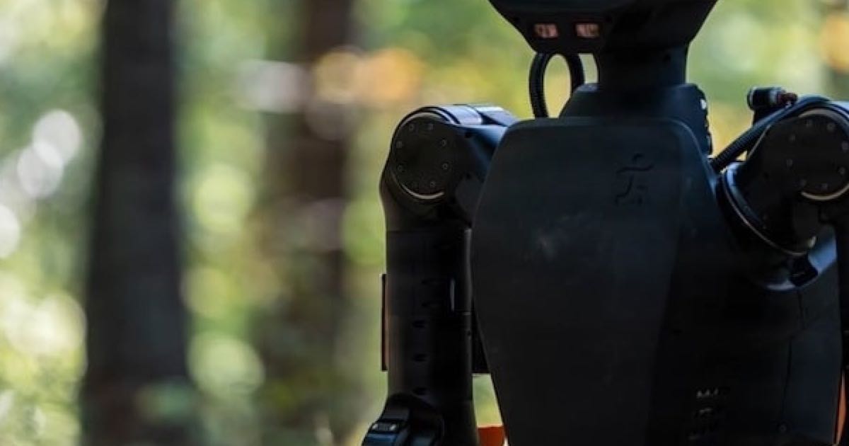 IHMC's Alex humanoid robot, a black-bodied biped with orange cabling at the joints, standing among trees