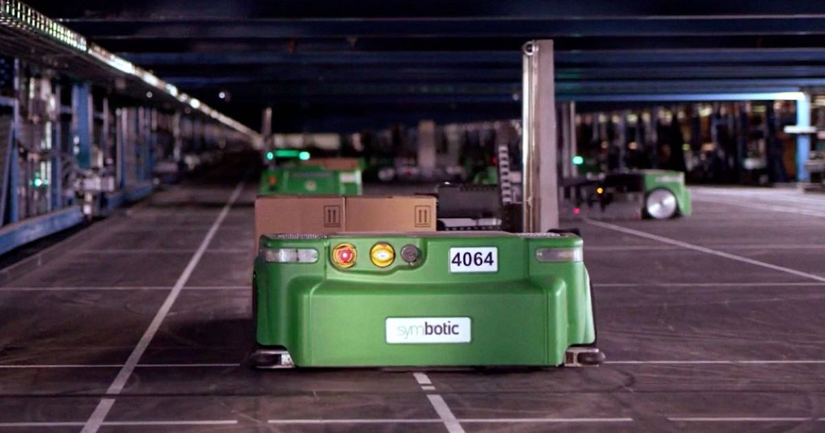 A green Symbotic wheeled warehouse robot carrying cardboard boxes inside a Walmart automated distribution facility